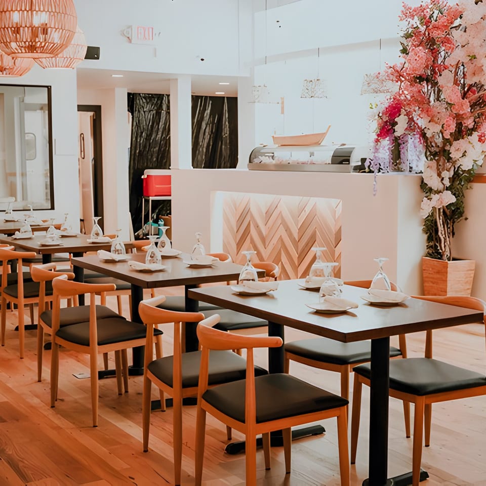 Bleu Ginger's dining room with set tables, wooden chairs, and a floral arrangement near the sushi bar.