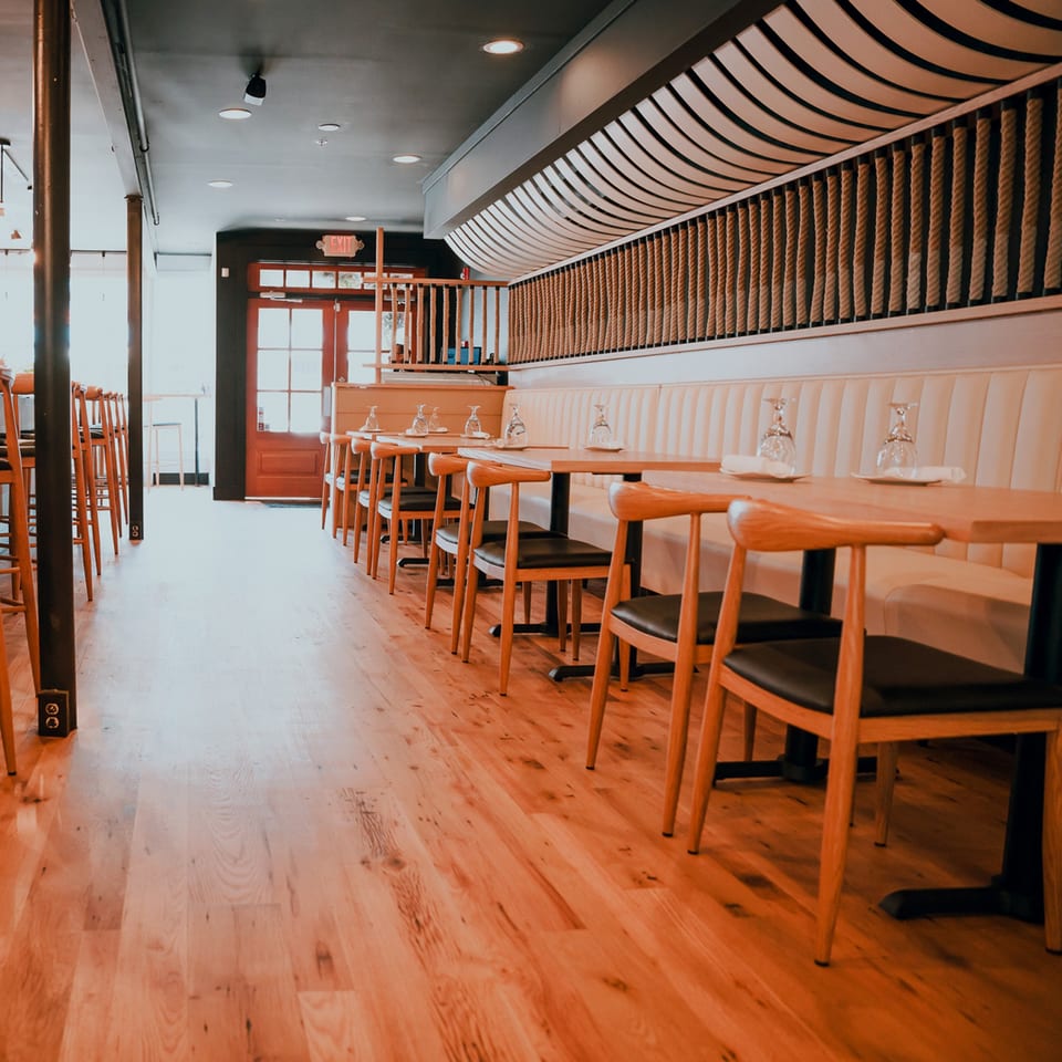 Interior of Bleu Ginger restaurant with wooden tables, chairs, and a long cushioned bench along the wall.