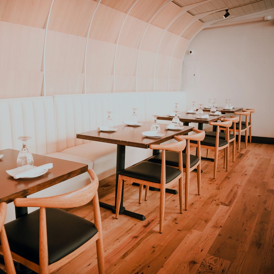 Bleu Ginger's dining room with light wood tables, chairs, and booth seating, set with glasses and plates.