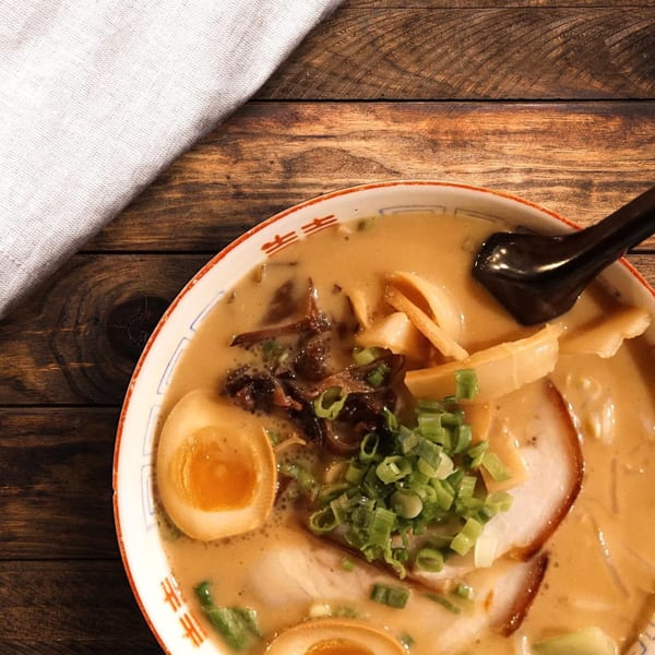 Bleu Ginger's ramen bowl with pork, egg, scallions, and mushrooms on a wooden table.