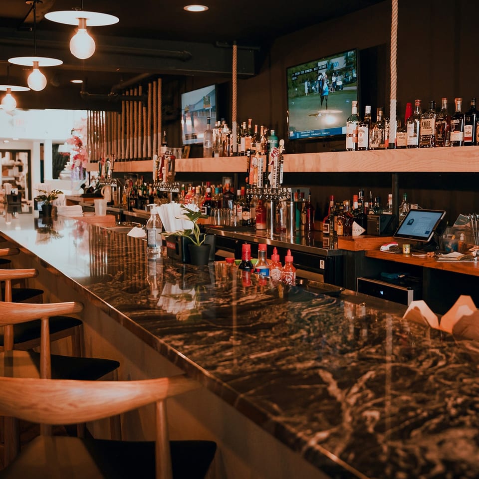 A long, dark marble bar with wooden stools, liquor bottles, beer taps, and TVs showing golf.