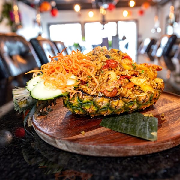 Pineapple fried rice with shrimp, carrots, and cucumber served in a pineapple half on a wooden board.