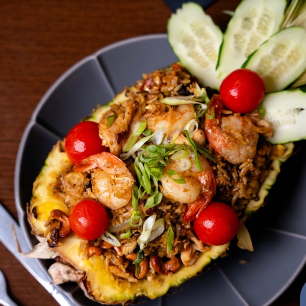Pineapple fried rice with shrimp, cashews, cherry tomatoes, and scallions, garnished with cucumber slices.