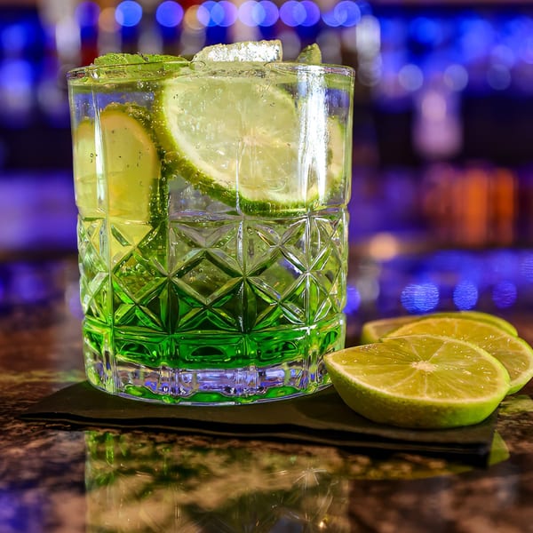 A vibrant green cocktail with lime slices and mint in a textured glass on a bar.