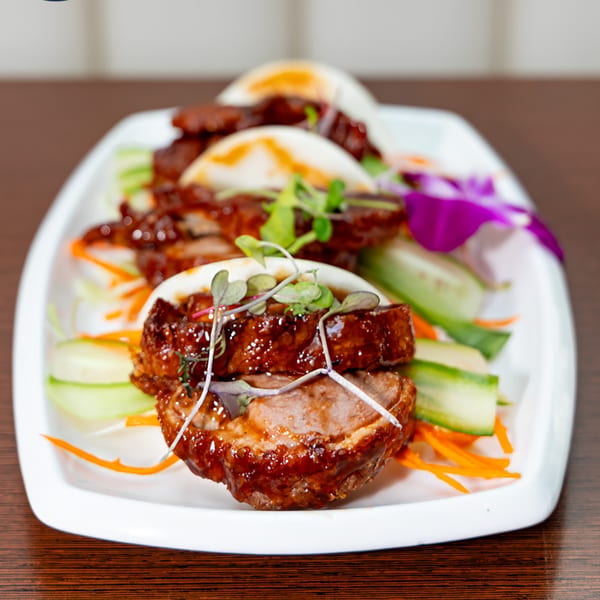 Bleu Ginger's duck bao buns with microgreens, cucumber, and shredded carrots on a white plate.