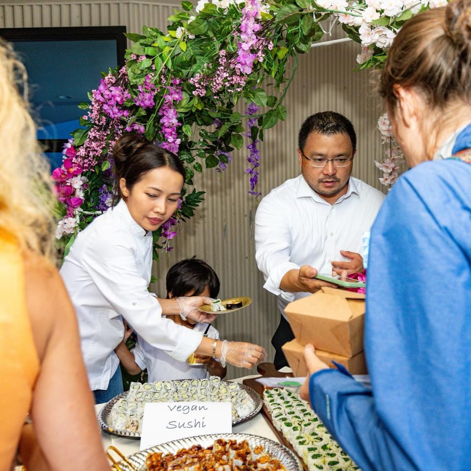 Bleu Ginger staff serving vegan sushi to guests from a buffet table decorated with flowers.